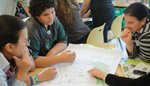 adults and children gather around a table where a map is laid out.