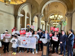 A large group assembles around a podium at the New York Capitol. Many are holding red and white signs that read, "Make basement apartments safe" and "Legalize Basement apartments." Other signs read "CUFFH." A large banner being held by several people reads "Remembering Lives Lost to Hurricane Ida"