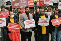 Advocates from BASE coalition stand together holding signs reading "Legalize Basement and Cellar Apartments" and "Make basement and cellar apartments safe" in bold lettering.