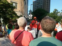 Rally participants listen in as a Justice for All coalition member holding a microphone addresses a crowd