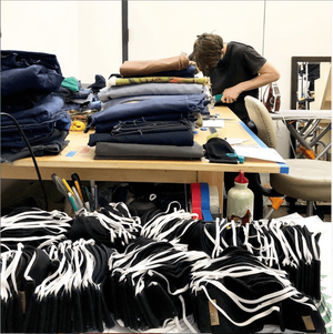 Man works at a table in background next to piles of fabric and newly made face masks