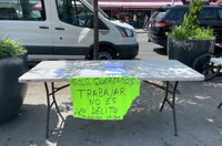 A neon green sign taped to a folding table reads in Spanish: "We only want to work. It is not a crime. Workers United."